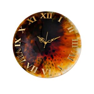 "A round handcrafted resin wall clock featuring a high-gloss finish with a central burst of deep amber, orange, and black fluid art. The clock face includes raised gold Roman numerals and ornate gold-toned filigree hands."
